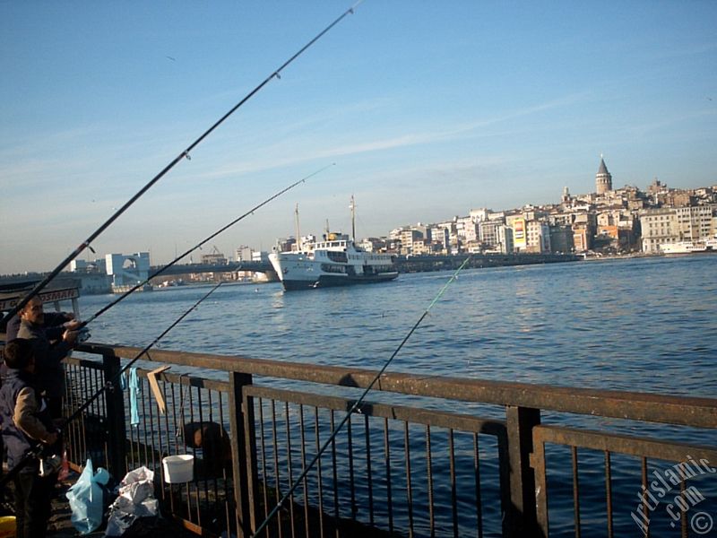 View of fishing people, a landing ship, Galata Bridge and Galata Tower from the shore of Eminonu in Istanbul city of Turkey.
