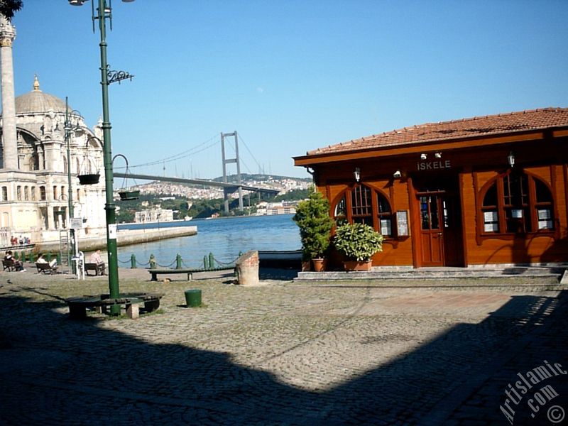 View of the jetty, Bosphorus Bridge, Ortakoy Mosque and the moon seen in daytime over the bridge`s legs from Ortakoy shore in Istanbul city of Turkey.

