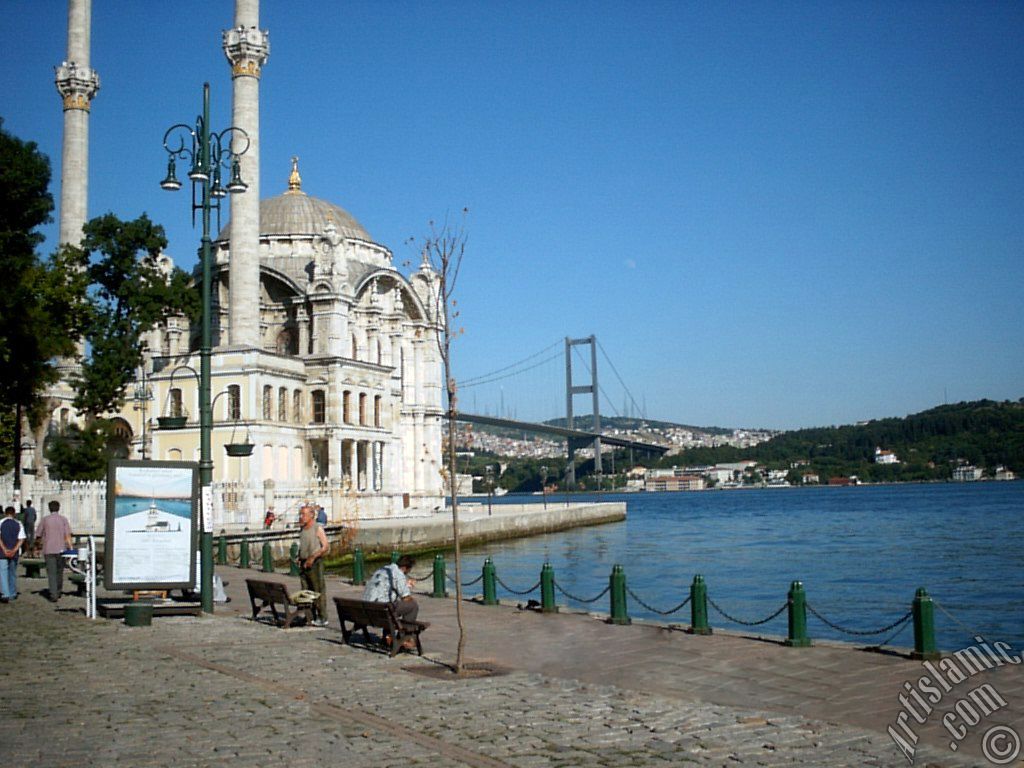 View of Bosphorus Bridge, Ortakoy Mosque and the moon seen in daytime over the bridge`s legs from Ortakoy shore in Istanbul city of Turkey.

